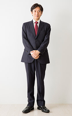 【身だしなみの見本】濃いグレーのスーツ、白シャツ、赤いネクタイ、黒い革靴を着用